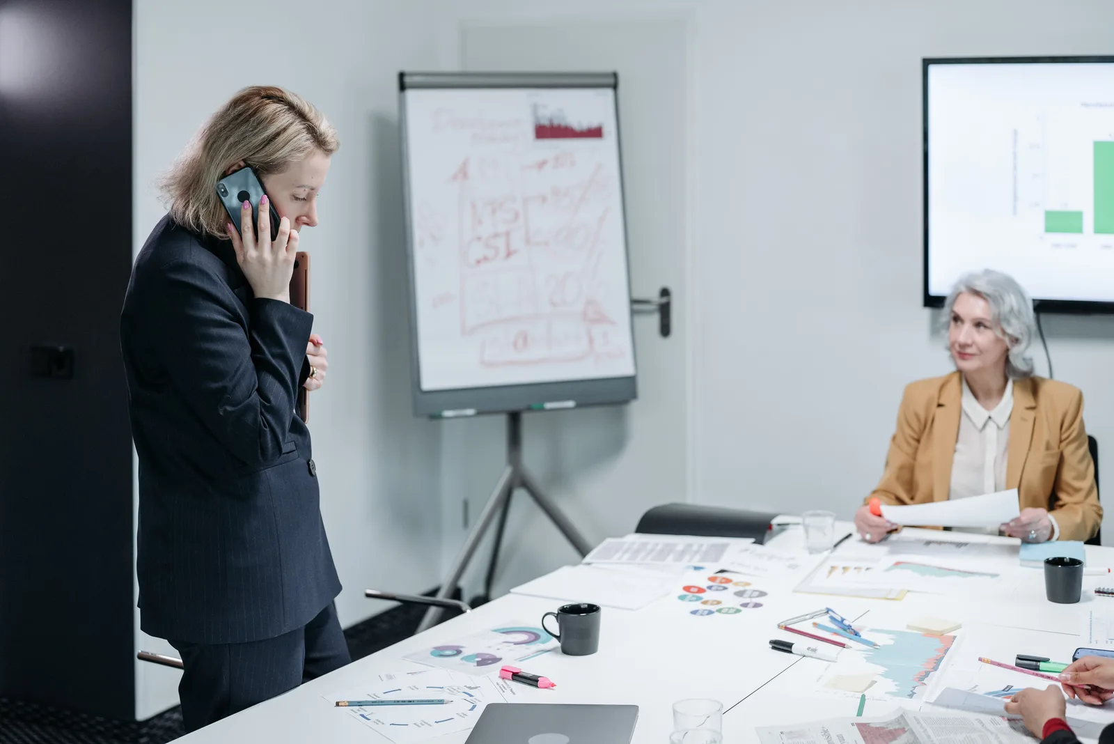 Two businesswomen in a meeting, discussing a project with charts and graphs.