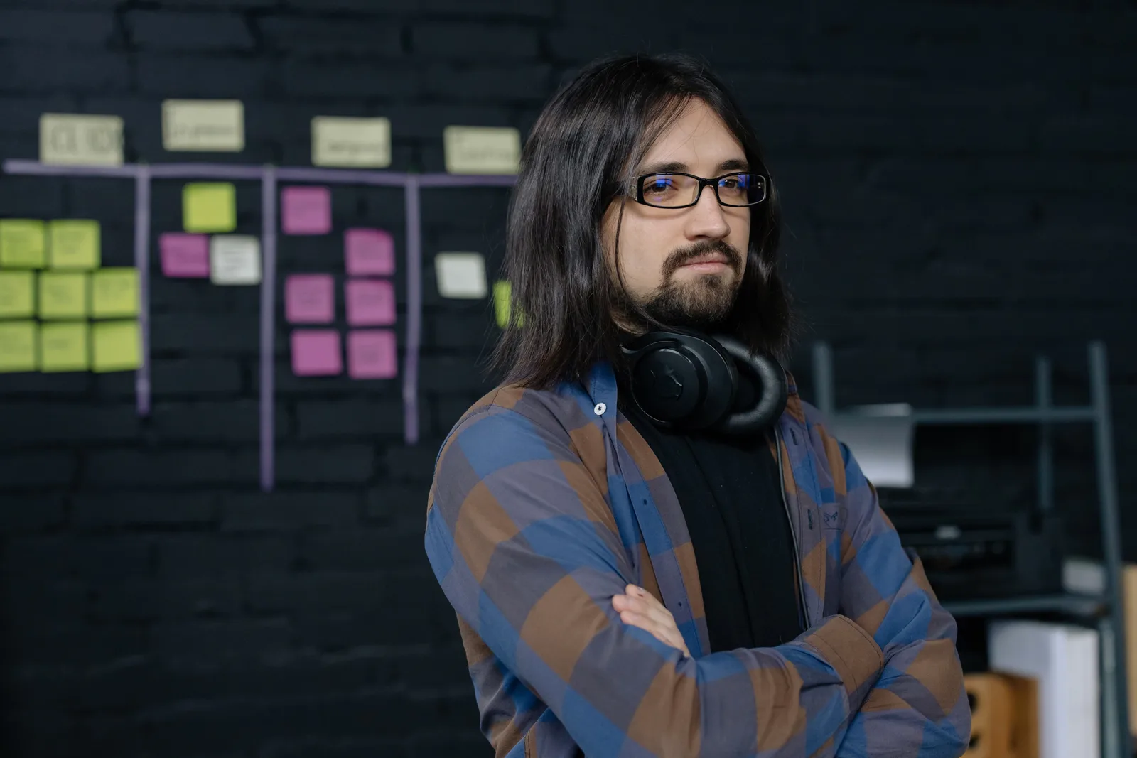 Portrait of a confident IT professional with headphones, standing in a modern office with sticky notes.